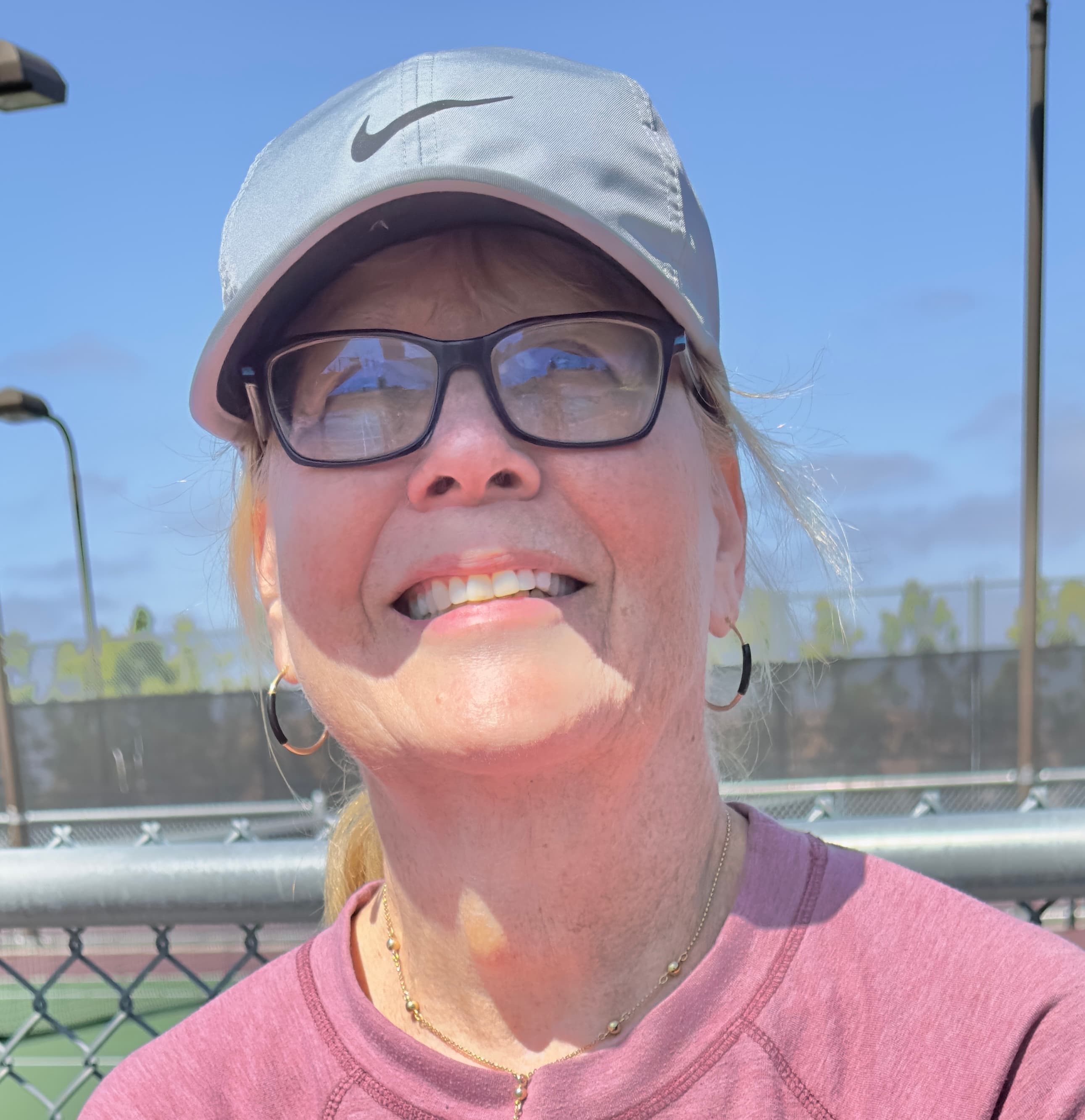A coach beams warmly in a close-up, cap and sunglasses on.