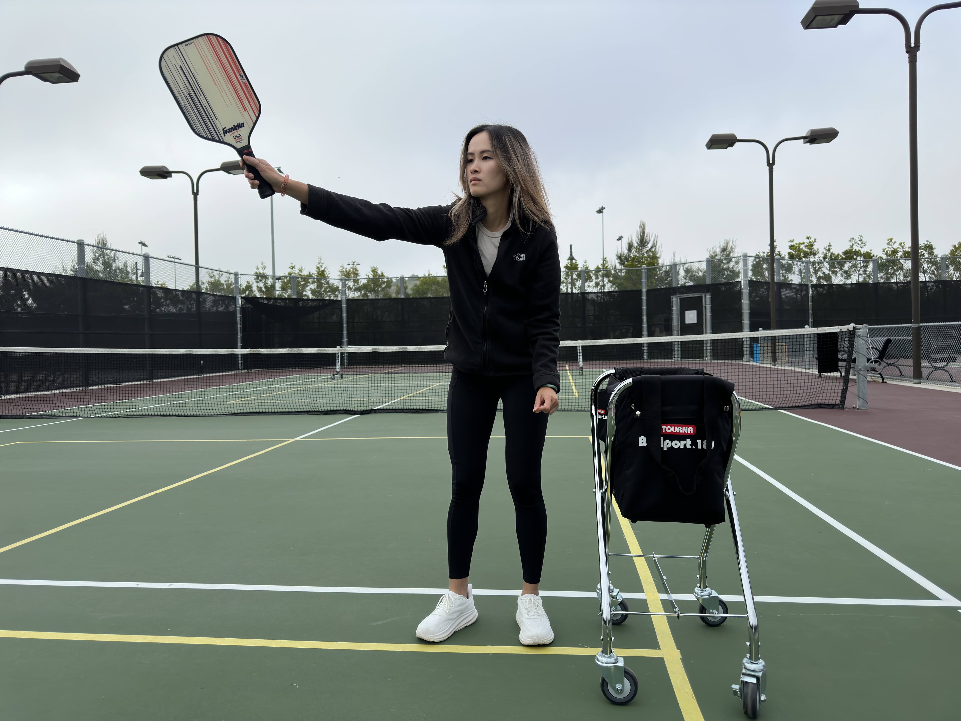 A coach extends her paddle in a poised, welcoming stance on court.
