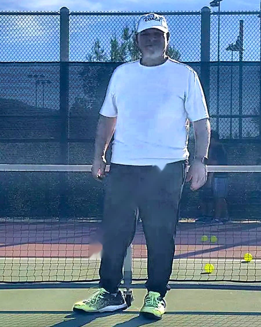 Coach Tobin mid-clinic on his home courts — net behind him, balls everywhere.